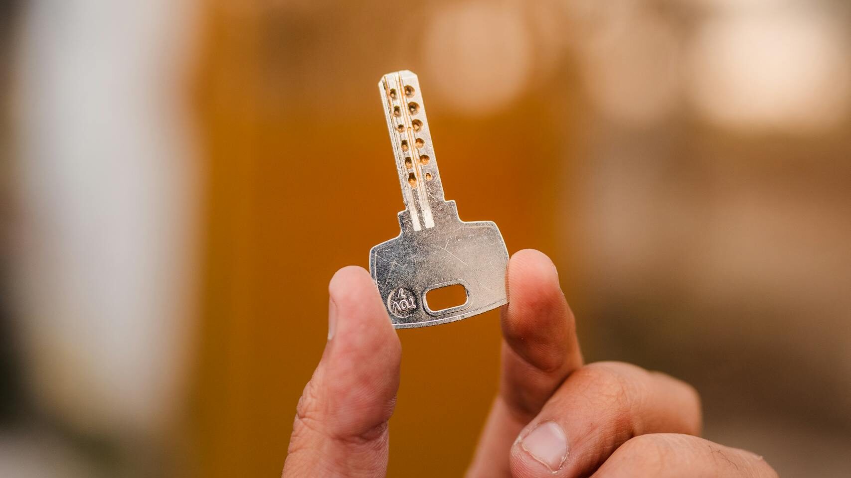 A detailed close-up of a hand holding a security key, with a blurred outdoor background.